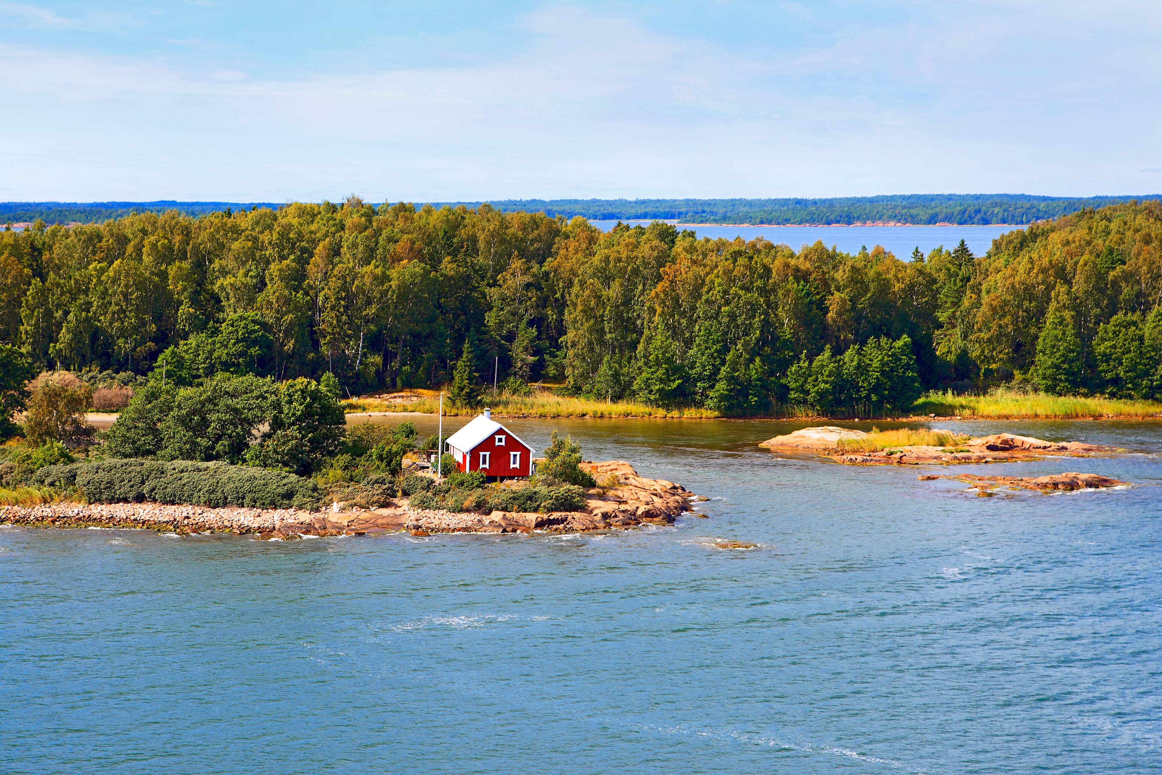 Een eiland met groene bomen en een klein rood huisje aan de oever van het meer.