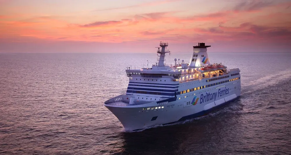 Ein Schiff von Brittany Ferries gleitet bei Sonnenuntergang über das ruhige Meer.