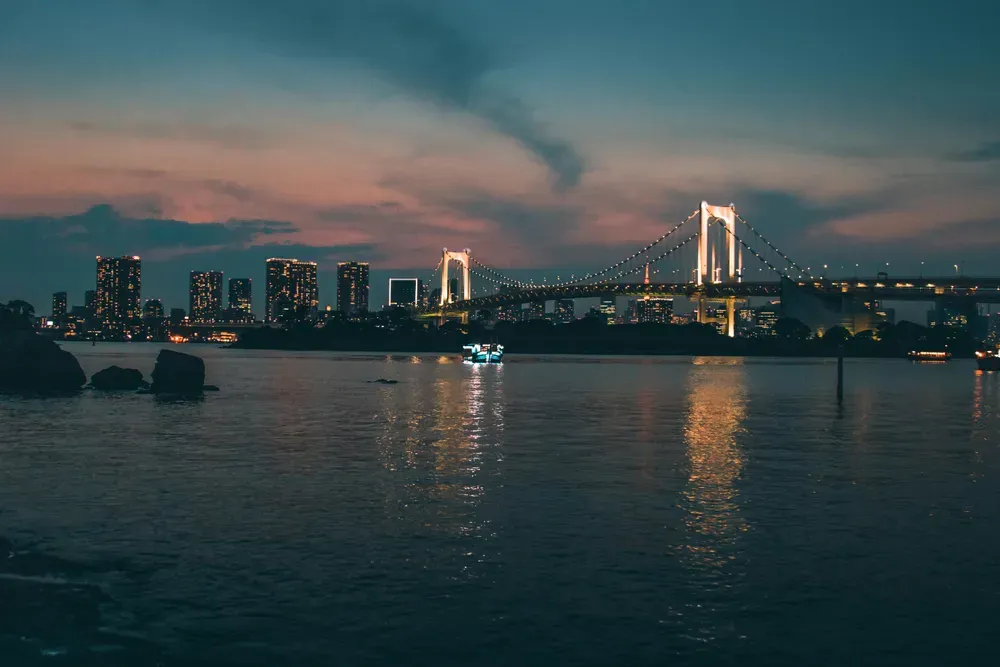 Die Bucht von Tokio kurz nach Sonnenuntergang. Das Wasser ist ruhig, die Brücke ist beleuchtet.