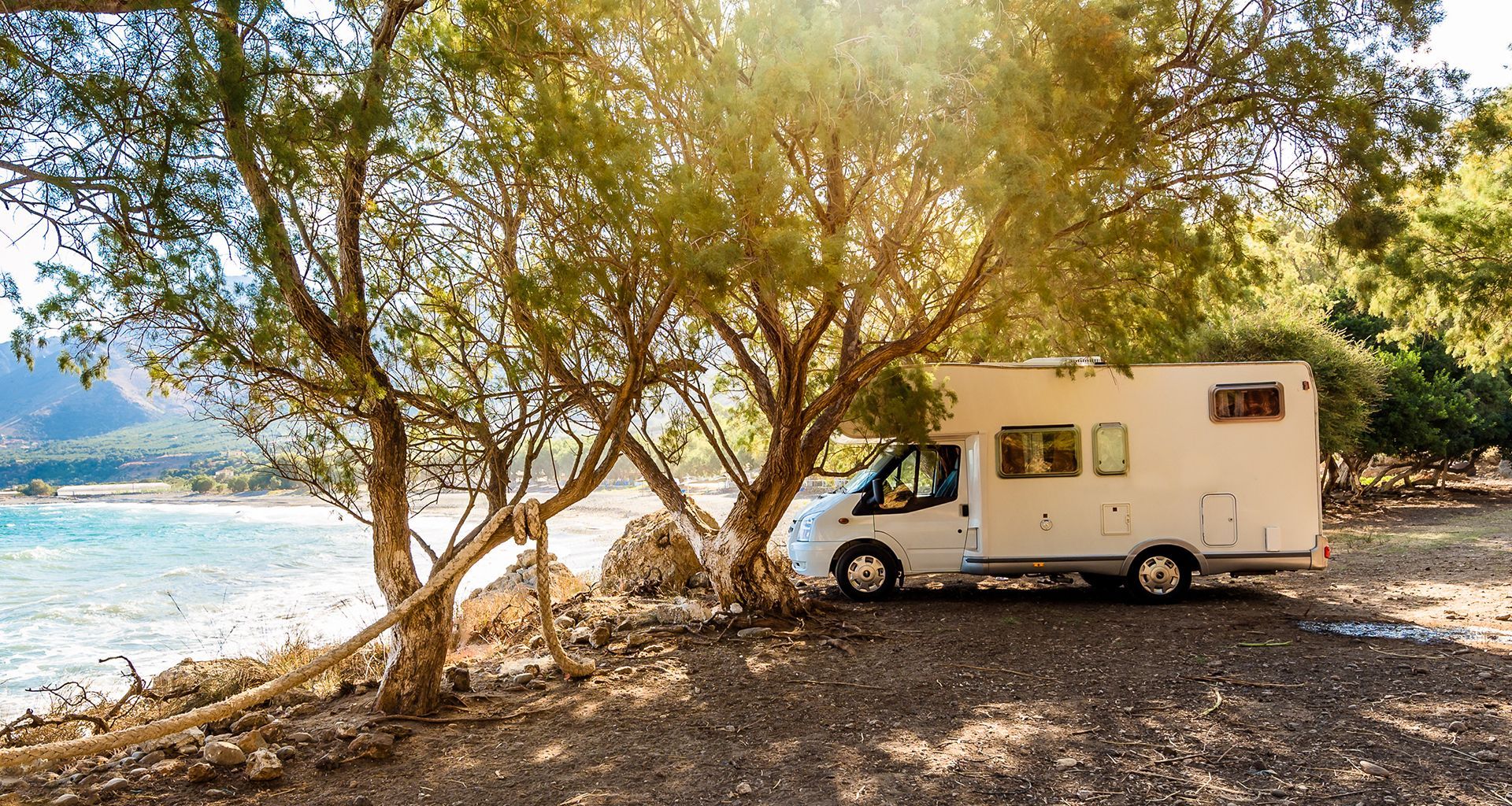 Een camper geparkeerd aan het meer onder bomen in de zon.