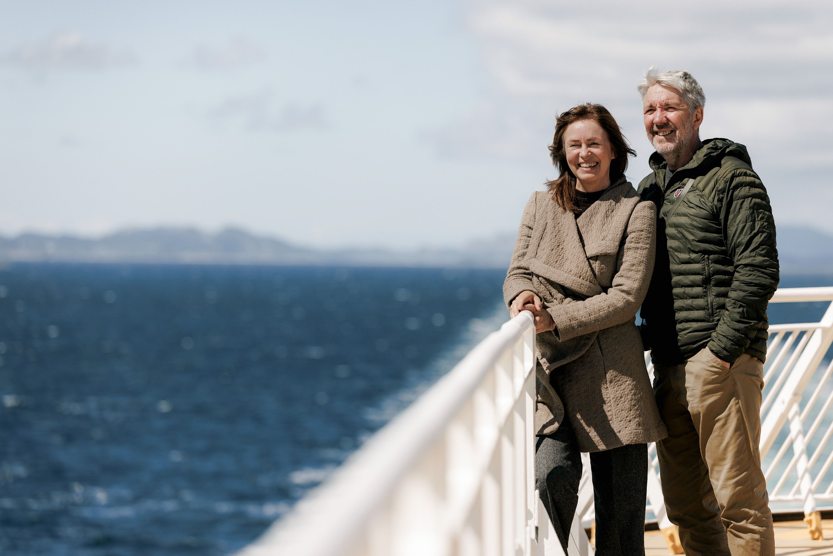 Un uomo e una donna sono sul ponte di un traghetto. Il sole splende ed entrambi ridono.