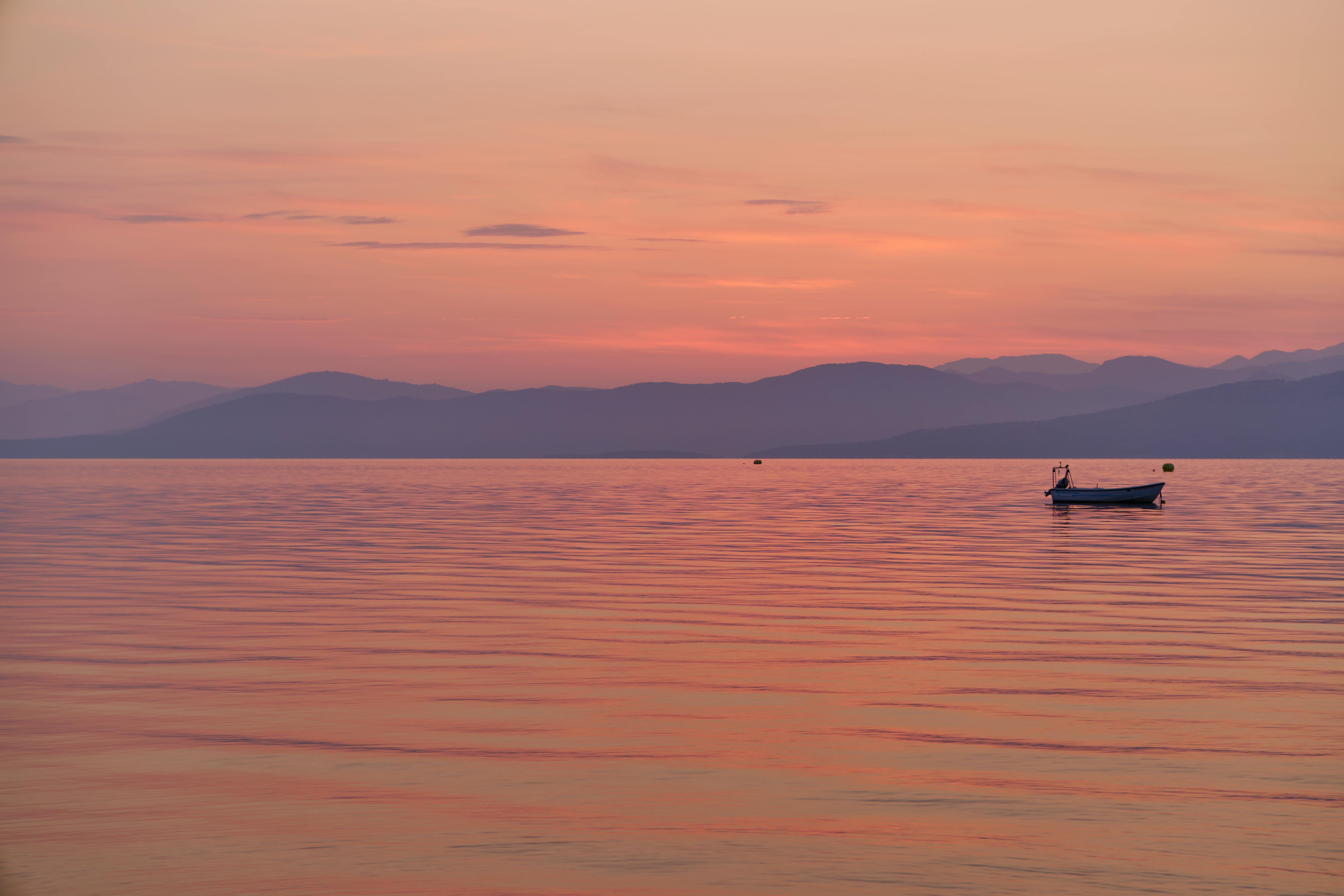 Tramonto rosa su Corfù con barchetta all'orizzonte.