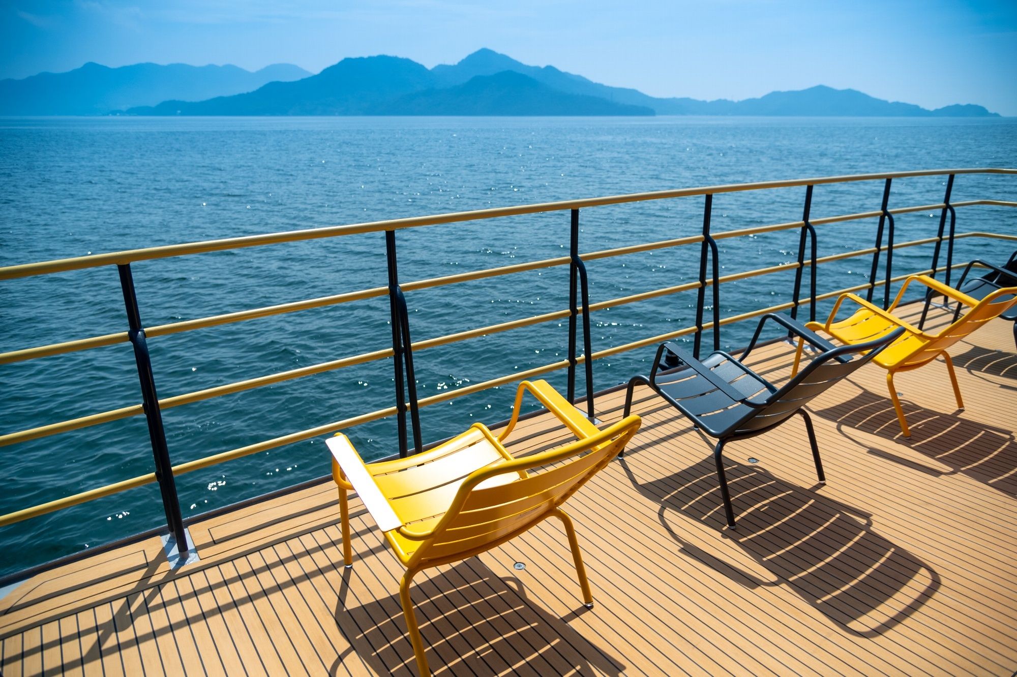 Un ensemble de trois chaises longues disposées face à la rambarde sur le pont d'un ferry, avec vue sur l'océan.