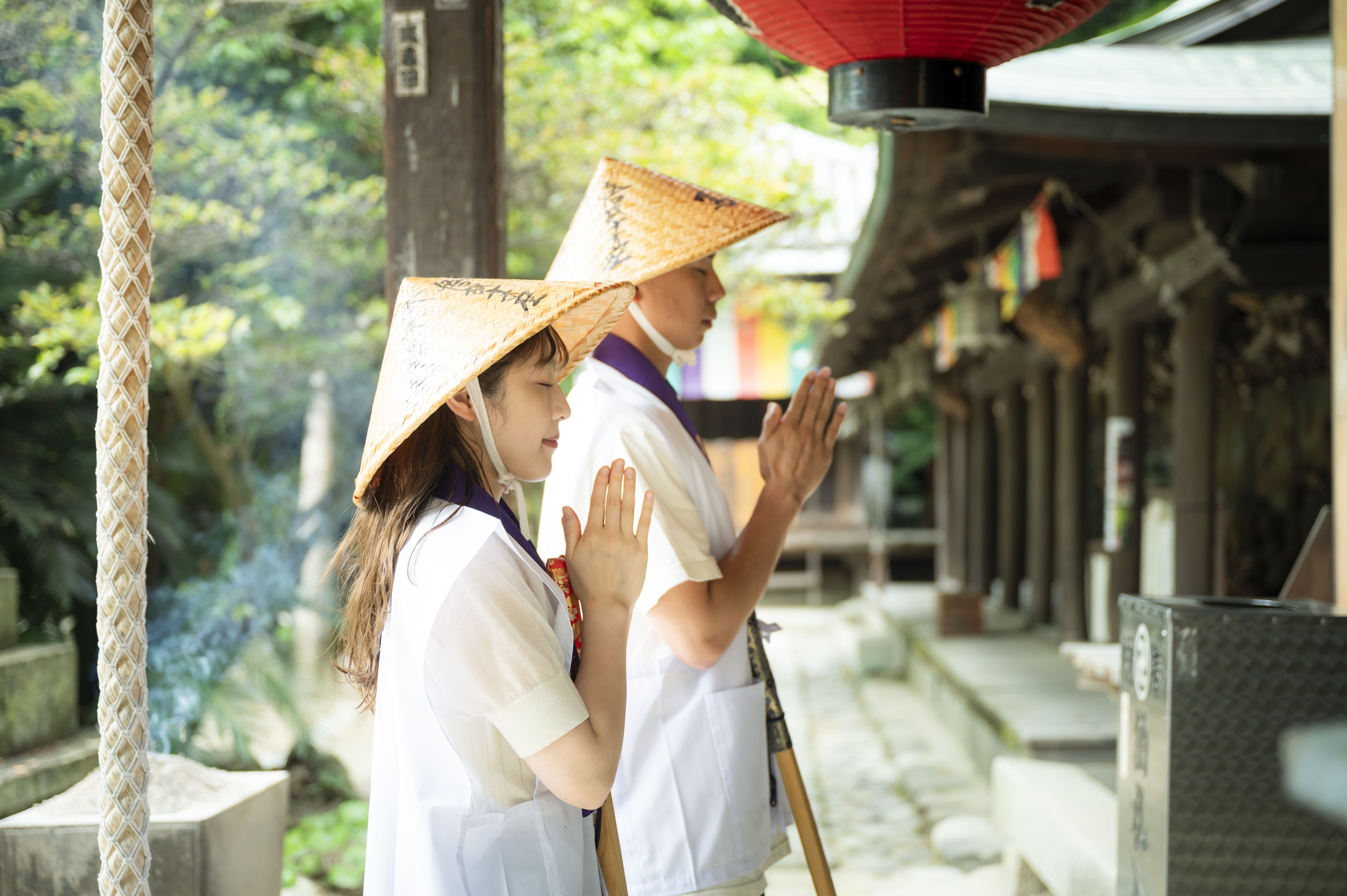 Two people in traditional outfits praying at at temple from the side.
