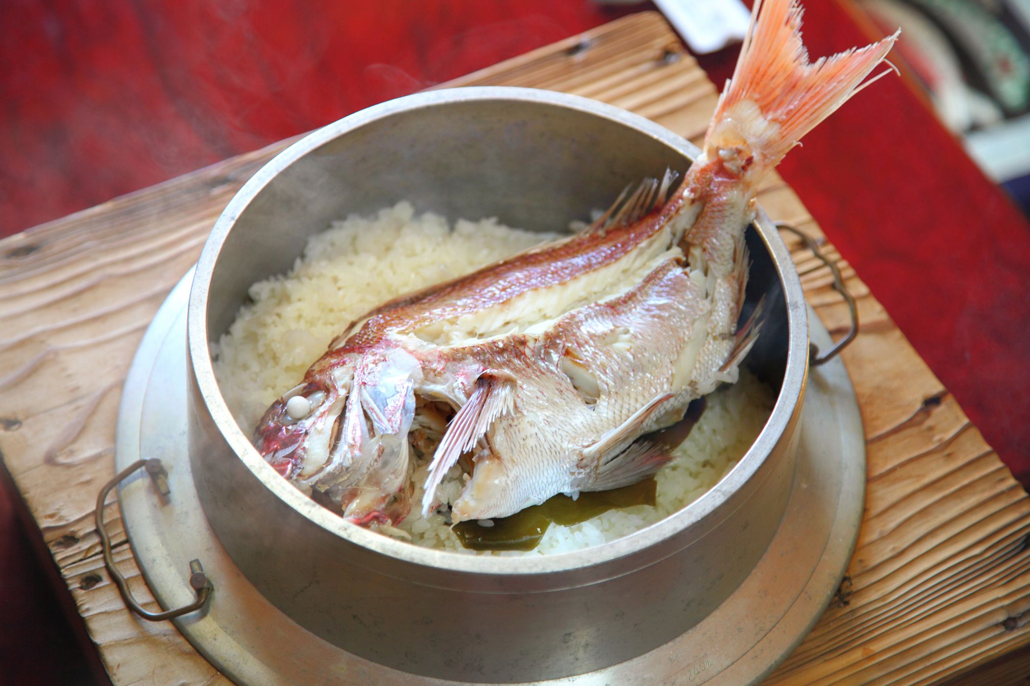 A steaming pot of rice with a fish on a wooden table.