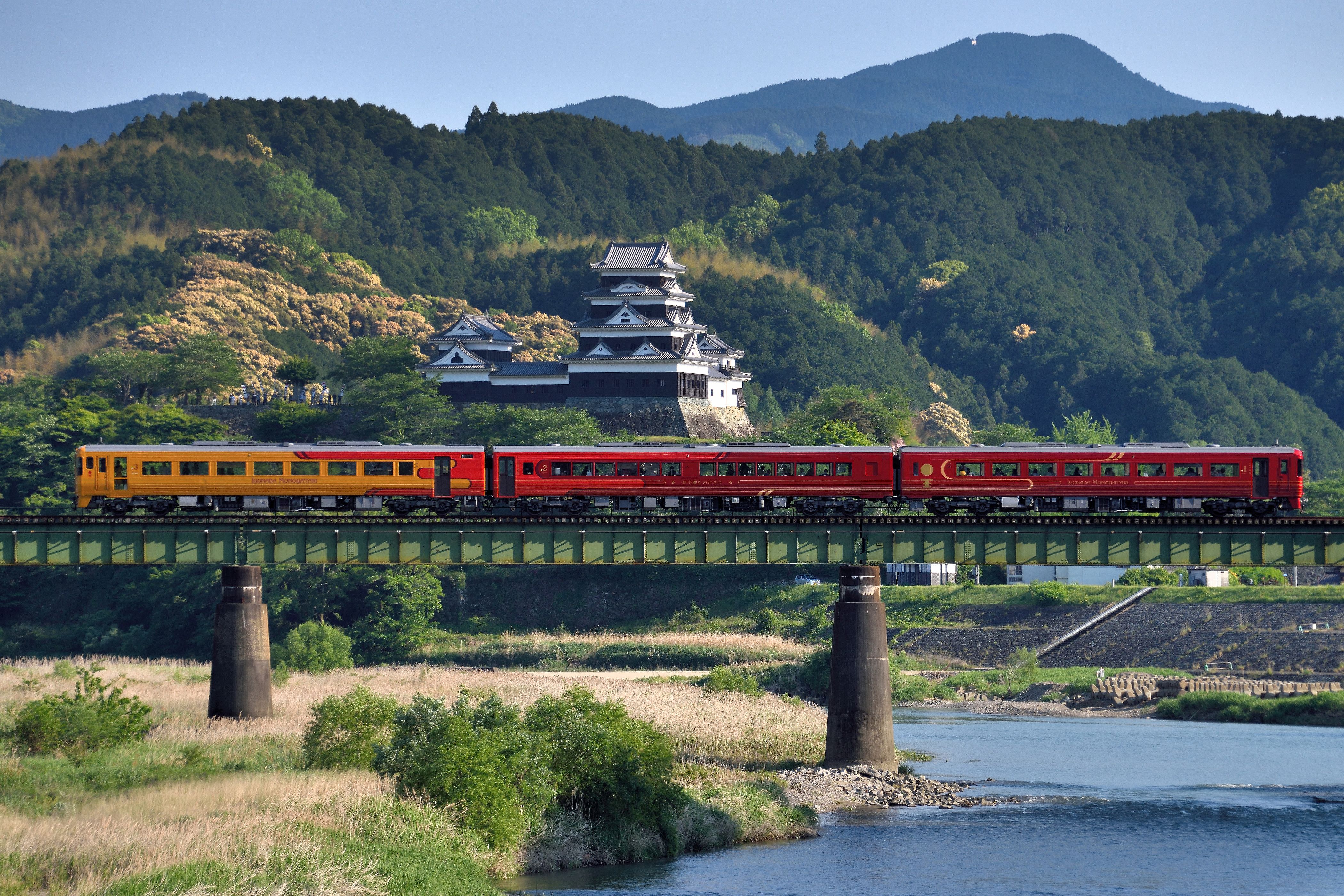Un train rouge sur un pont enjambant une rivière, avec des collines en arrière-plan.