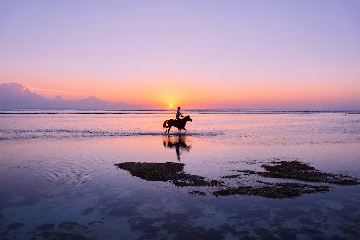 Eine Person reitet bei Sonnenuntergang am Strand von Gili Trawangan in Indonesien entlang.