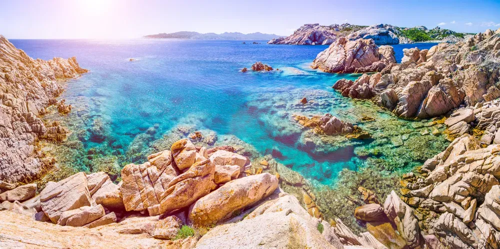 Die raue Felsküste von La Maddalena, Sardinien, ragt ins türkisfarbene Meer, das im Sonnenschein glitzert.