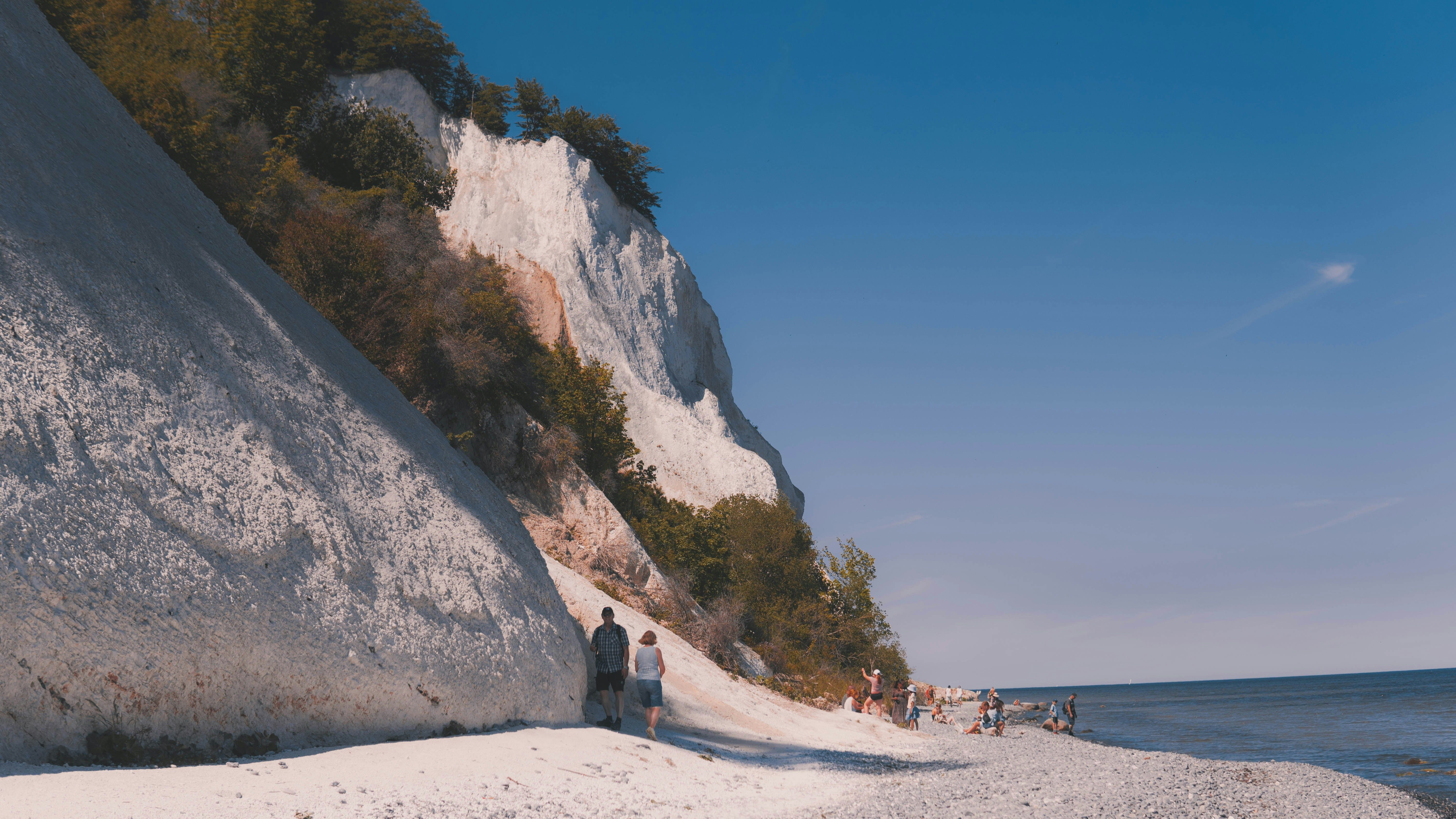 De witte kliffen van Mons Klint, een krijtrots in Denemarken. Je ziet een paar mensen aan de voet van de klif, die naar een klein strandje en uiteindelijk naar de zee leidt.