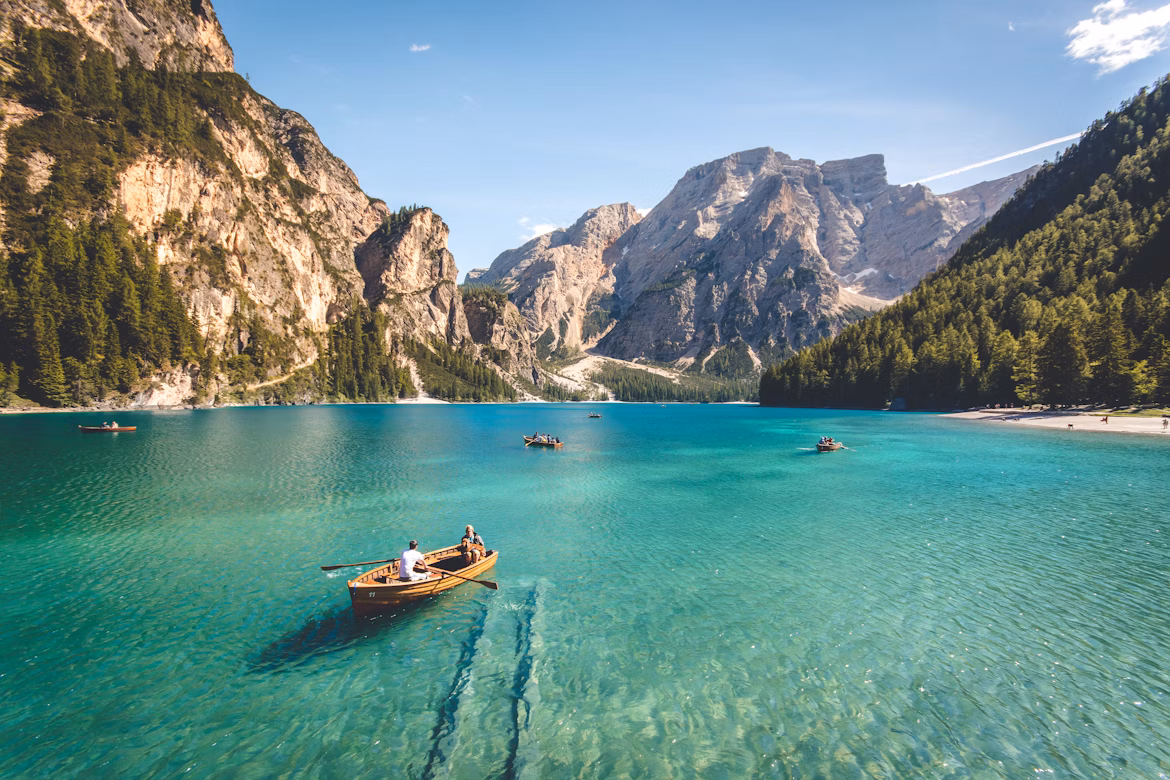 Het Pragser Wildsee-meer in Italië. Kristalhelder water, waarop een paar roeiboten te zien zijn, ligt voor indrukwekkende bergen.