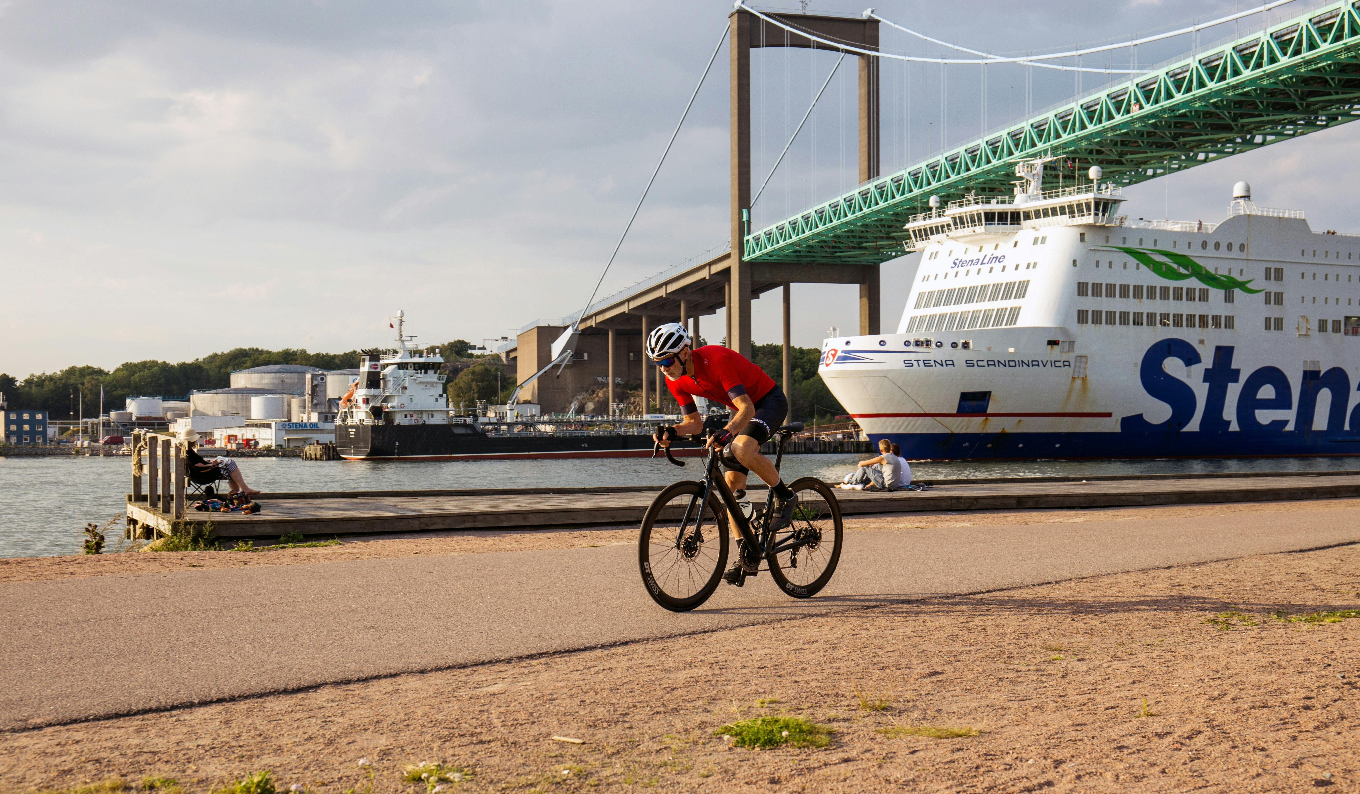 Ein Radfahrer fährt entlang der Uferpromenade in Göteborg, Schweden, entlang. Im Hintergrund sind die Älvsborg-Brücke und eine Fähre der Stena Line zu sehen.