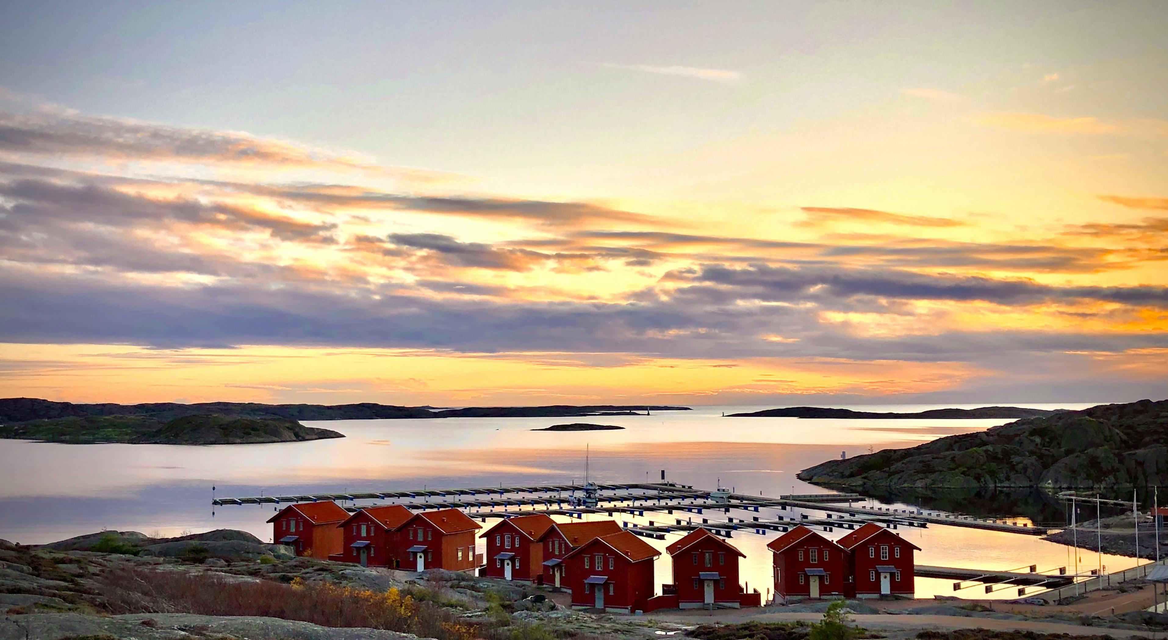 Bei Sonnenuntergang sieht man neun typisch schwedisch rote Häuser an einem ruhigen Wasser.
