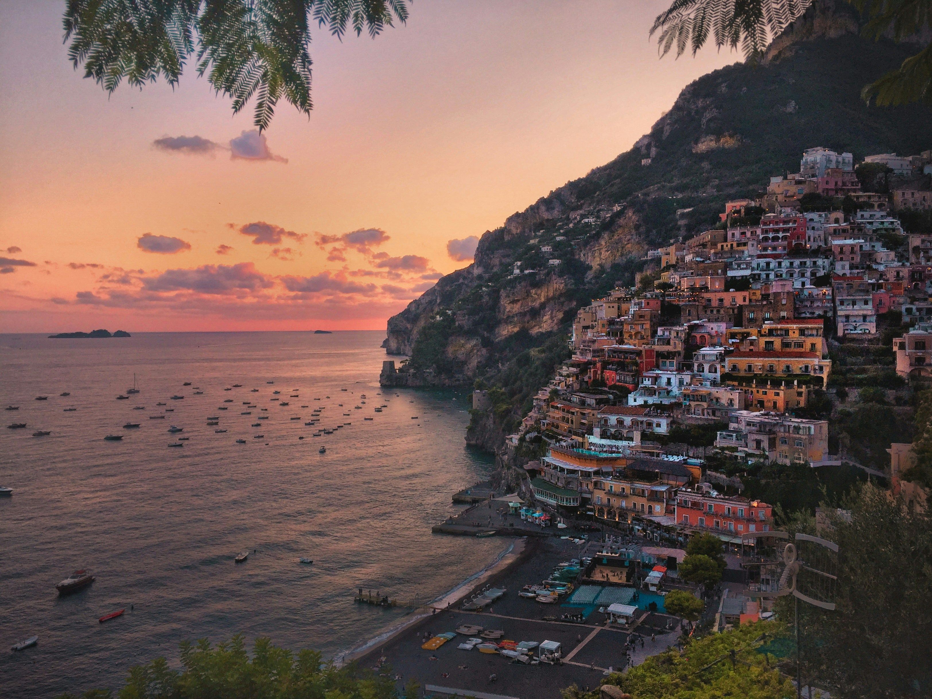 Die bunten Häuser von Salerno im roten Abendlicht des Sonnenuntergangs. Auf dem Meer tummeln sich noch einige Boote.