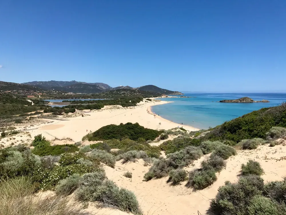Der Sandstrand Su Giudeu in Chia an der Südküste Sardiniens. Er erstreckt sich über Sanddünen, rechts im Bild sieht man die vorgelagerte kleine Insel Su Giudeu.