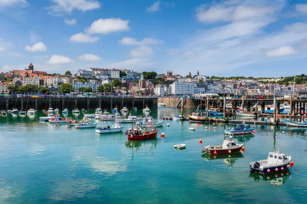 Das Hafenbecken St Peter Port in Guernsey mit einigen kleinen Booten strahlt in der Sonne und vor der Kulisse der Küste.