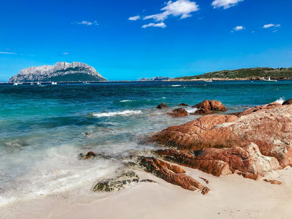 Wellen brechen sich am felsigen Strand von Alghero auf Sardinien.