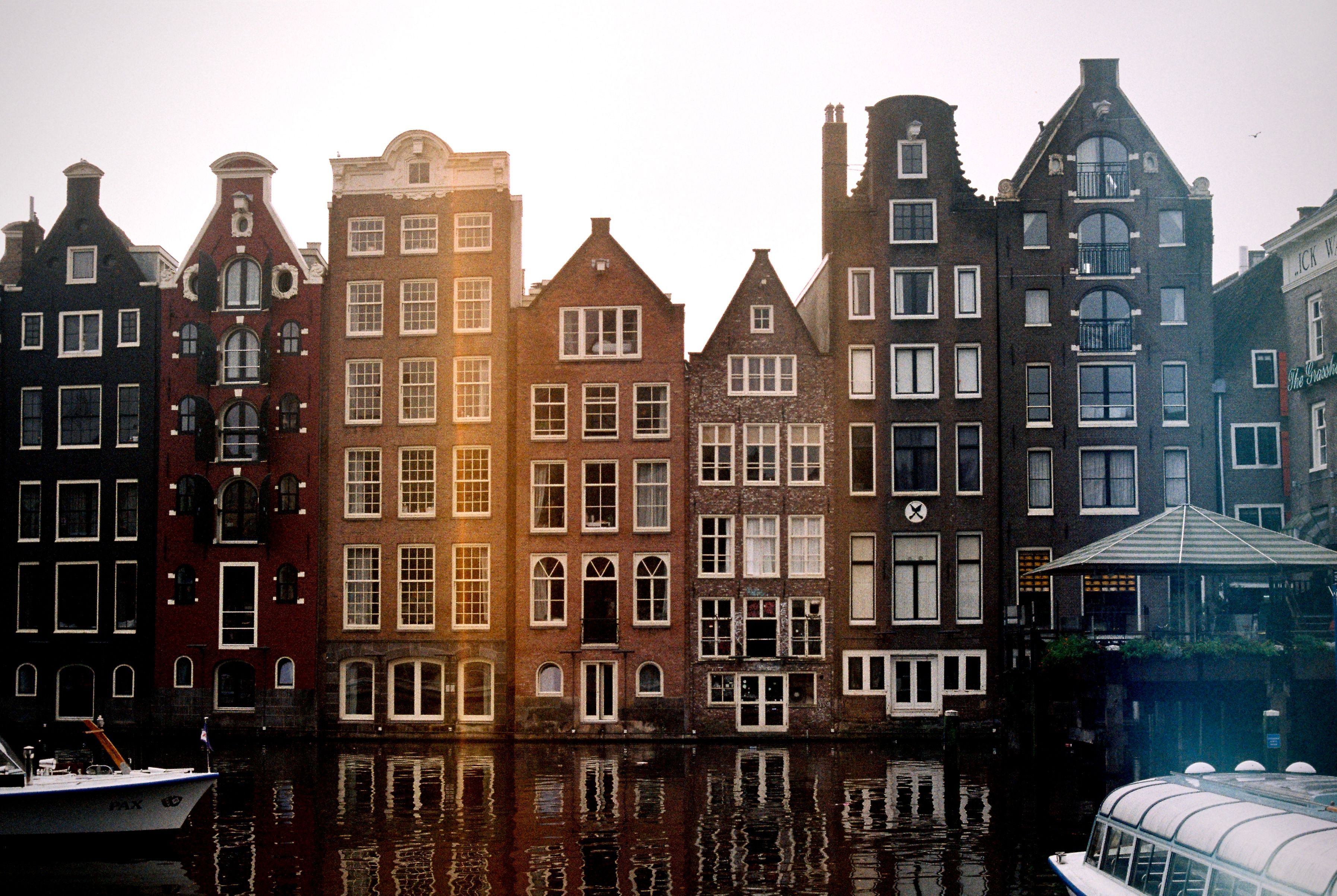 Die bunten „Tanzenden Häuser“ entlang des Damrak-Kanals in Amsterdam, die aufgrund ungleichmäßiger Setzungen ihrer Fundamente im Laufe der Jahrhunderte schief stehen.