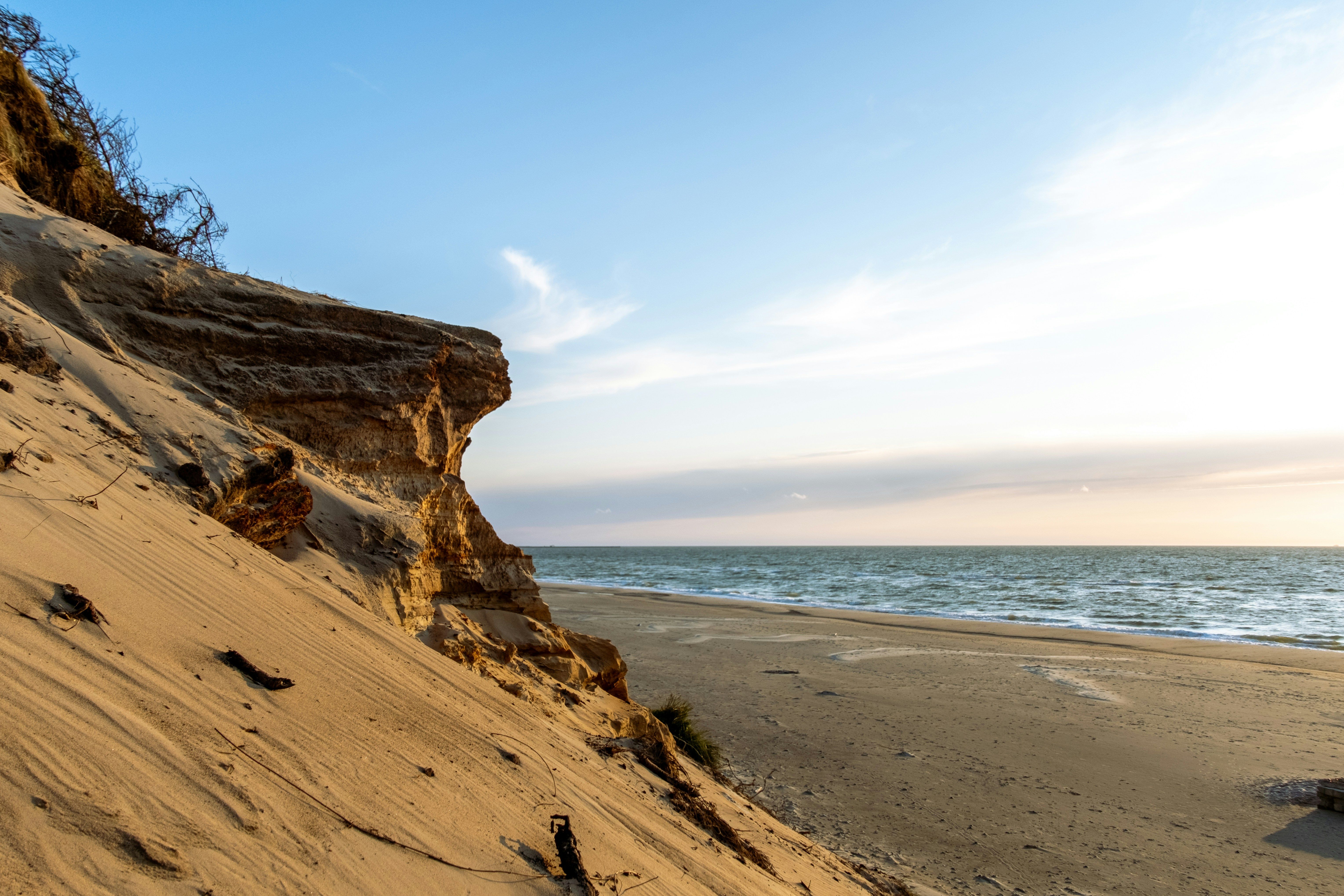 Die rauen Sanddünen des Thy-Nationalparks an der Westküste von Dänemark. Links sieht man die steil abfallende Düne, rechts den Strand und das Meer. Das Licht ist golden.