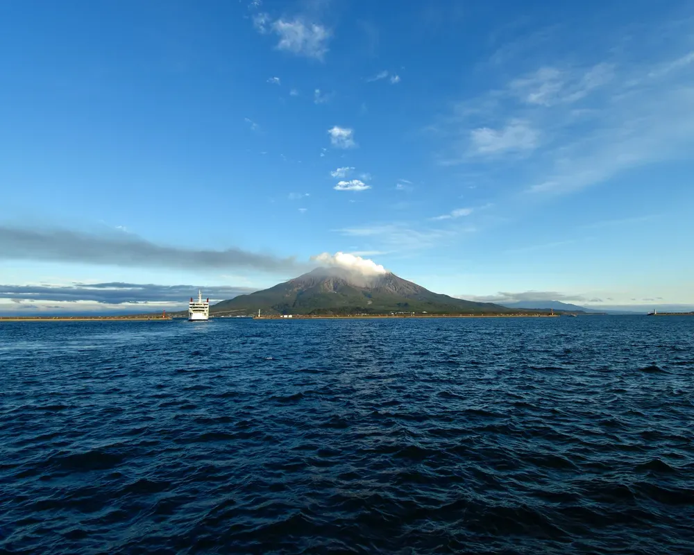 Eine Fähre legt in Sakurajima ab. Im Hintergrund sieht man den großen aktiven Vulkan auf der Halbinsel Sakurajima.