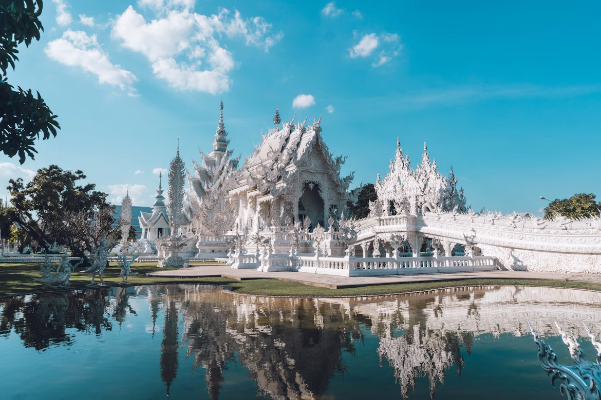 Der Weiße Tempel in Chiang Rai ist ein spektakuläres Gebäude, das sich im glatten Wasser spiegelt, während der sonnige, strahlend blaue Himmel lacht.