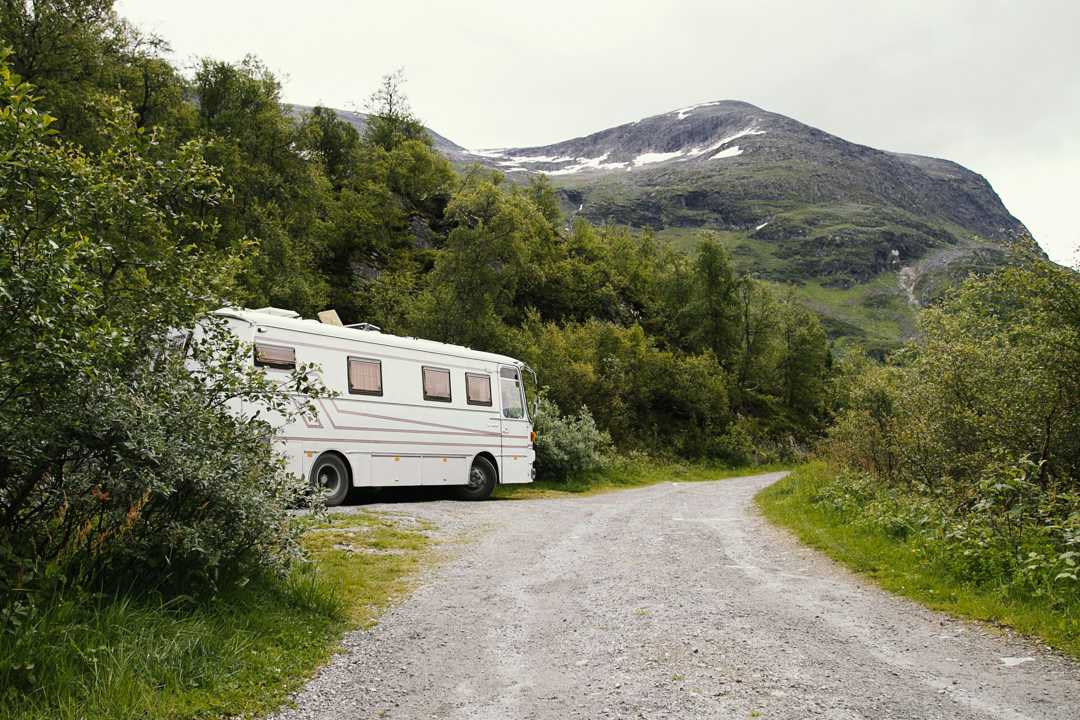 Ein weißes Wohnmobil steht in der einsamen Natur am Rand eines Schotterweges. Es ist von grüner Natur umgeben, im Hintergrund sieht man einen Hügel.