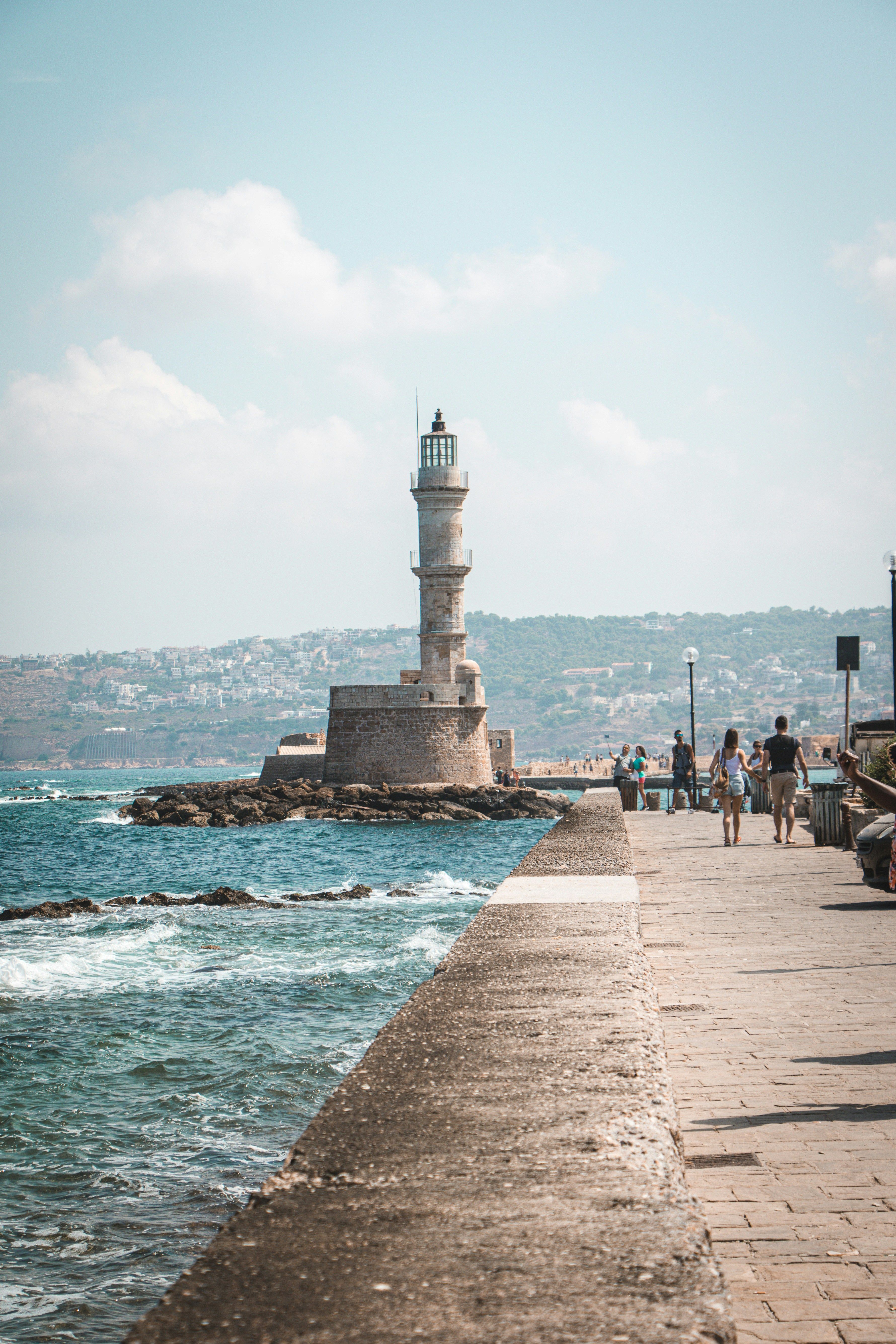 people walking towards lighthouse by the sea
