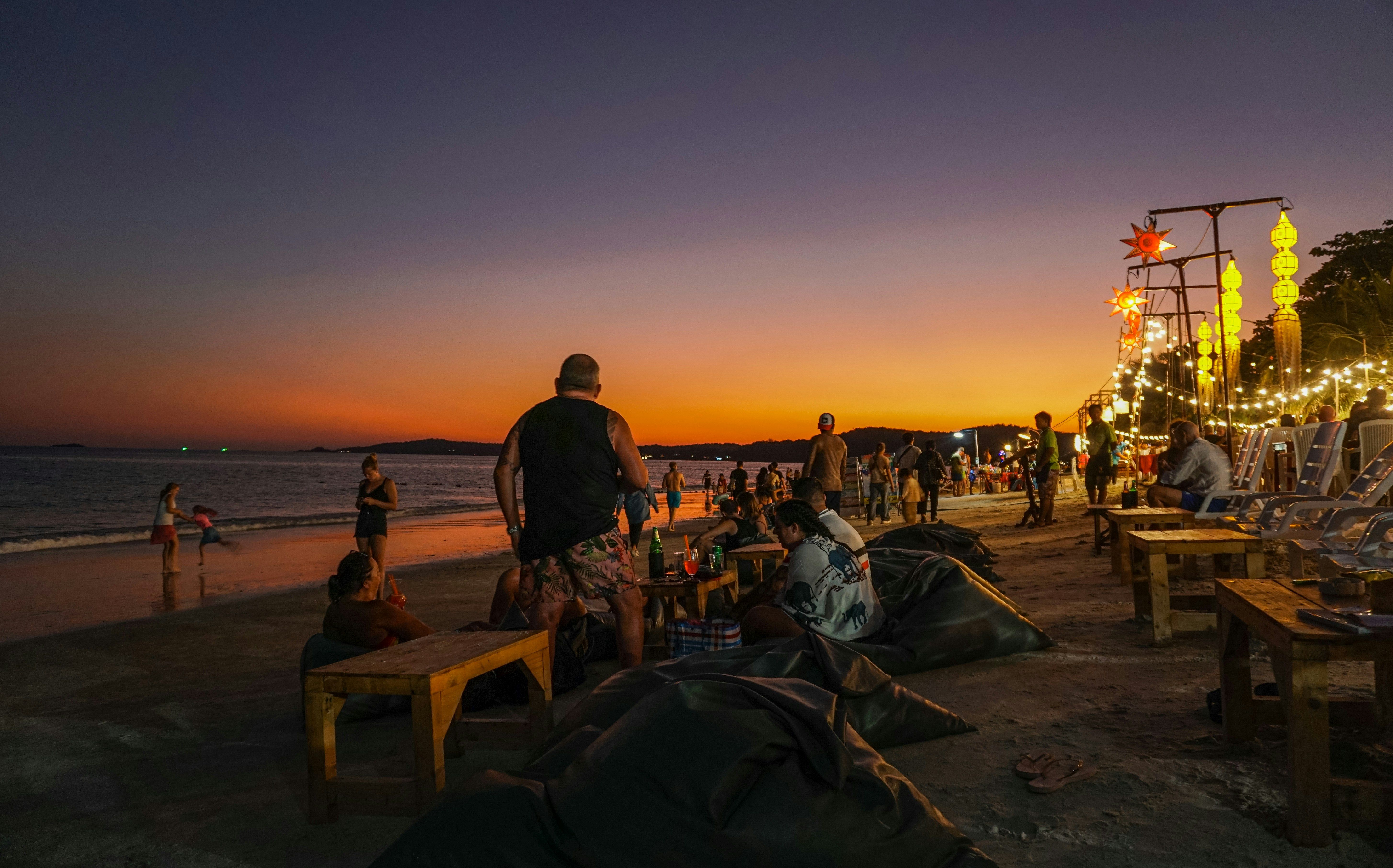 Zahlreiche Menschen kommen nach Sonnenuntergang am Strand zusammen und genießen die lebhafte Atmosphäre.