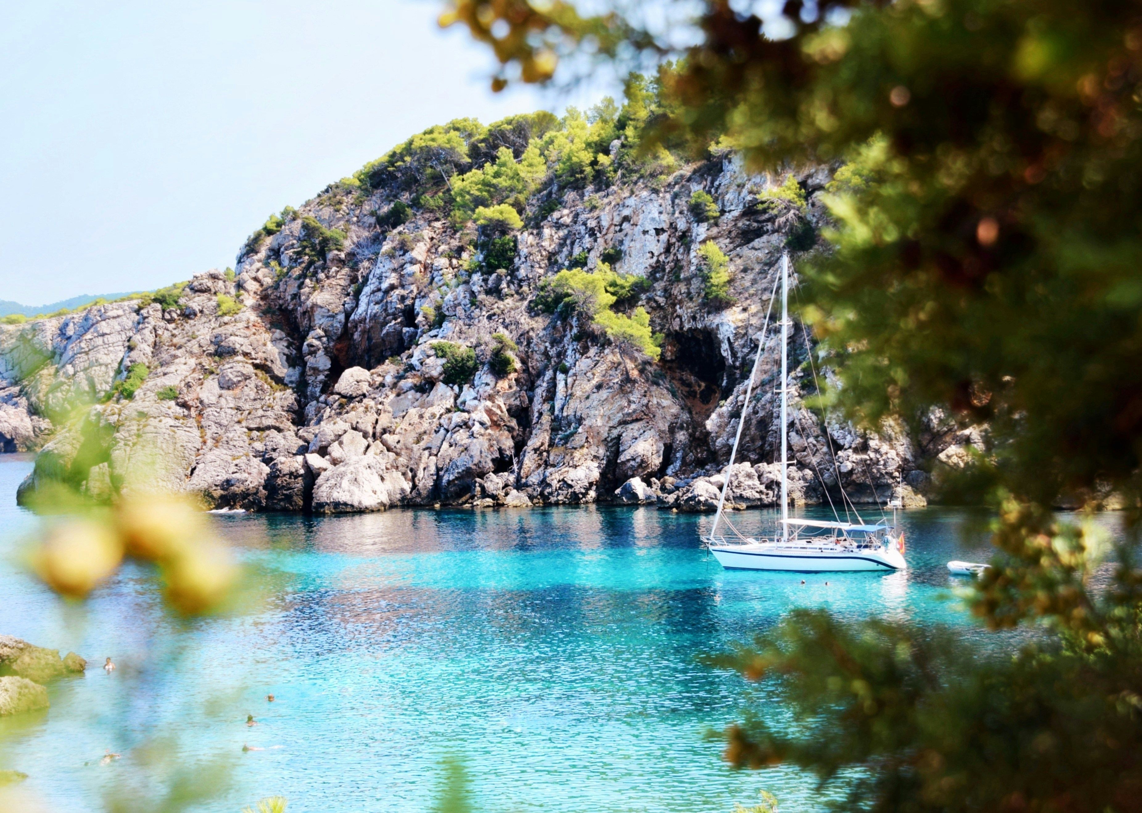 boat in blue sea surrounded by rocks in Ibiza
