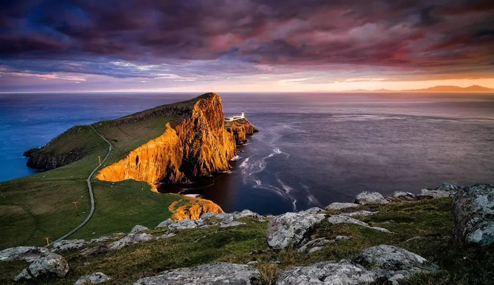 Acantilado iluminado por el atardecer en Neist Point, en la Isla de Skye, con el faro al fondo.