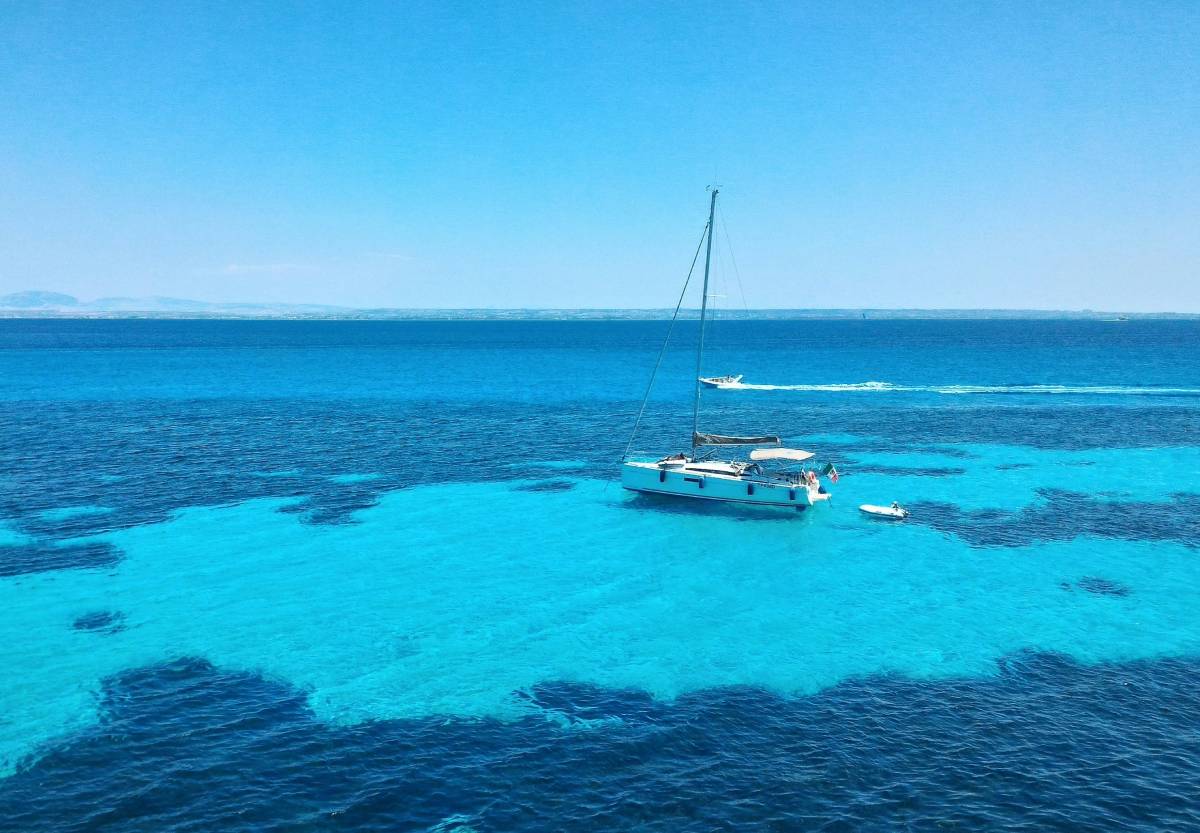 Catamarán anclado sobre aguas turquesas en la playa del Bue Marino, Favignana, en un día soleado
