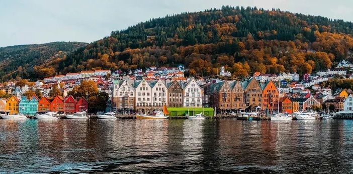 Vista panorámica del muelle de Bryggen en Bergen, Noruega, con casas de colores y colinas boscosas en otoño.