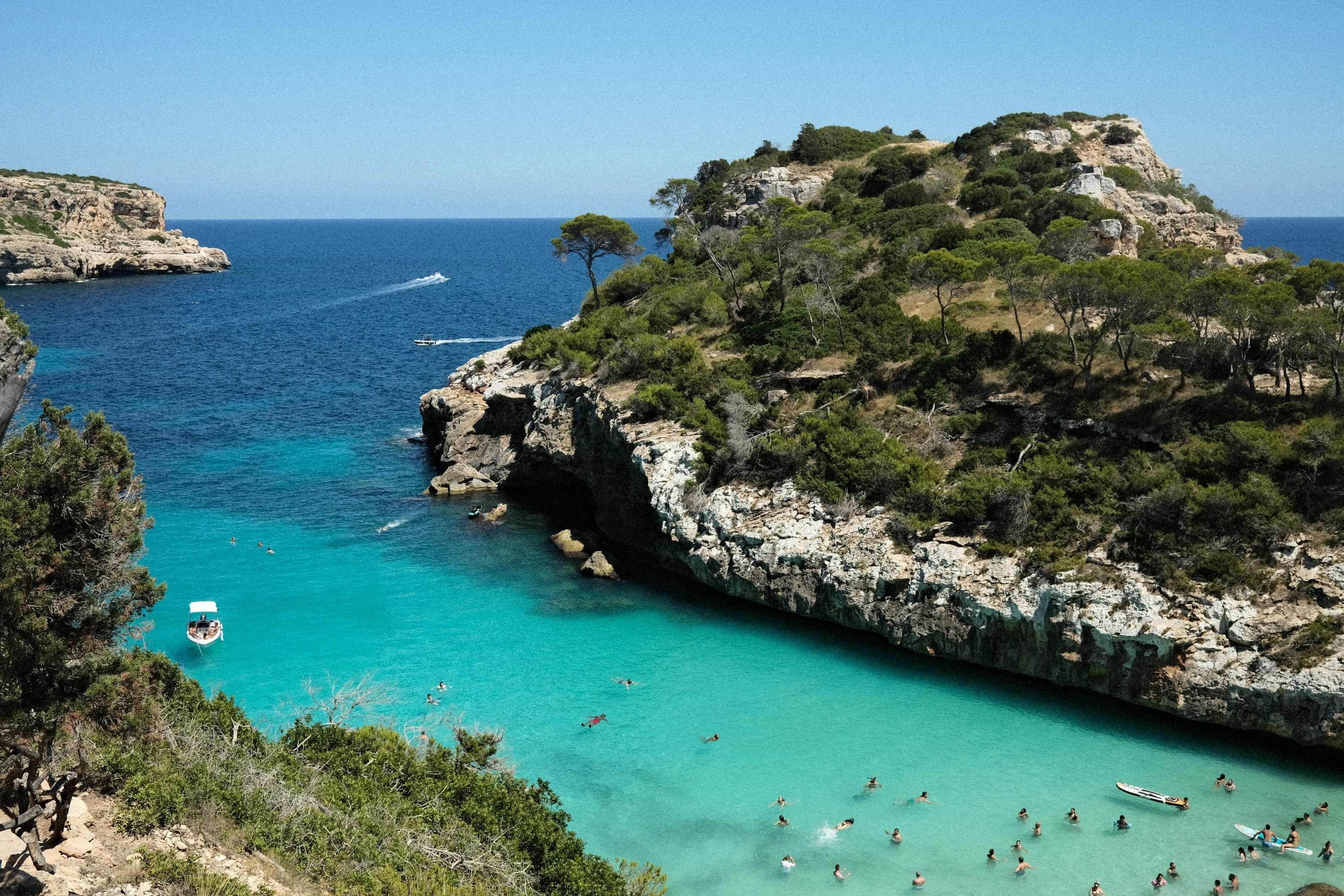 Vista aérea de Cala del Moro en Mallorca, España, con aguas turquesas, acantilados rocosos y bañistas disfrutando del mar Mediterráneo.
