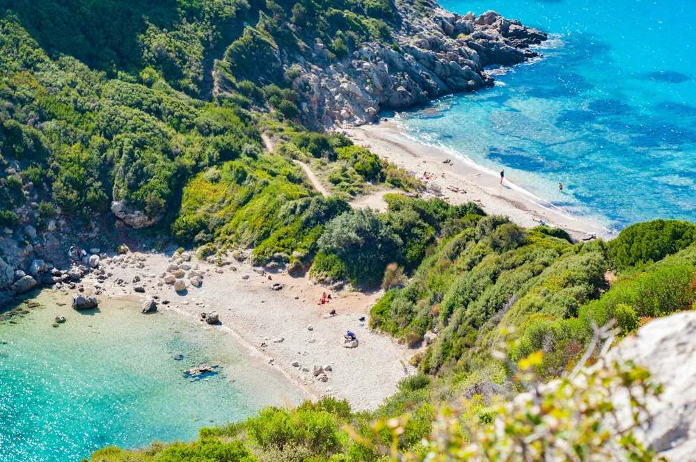 Playa escondida entre colinas verdes y aguas cristalinas en una cala del Mediterráneo.
