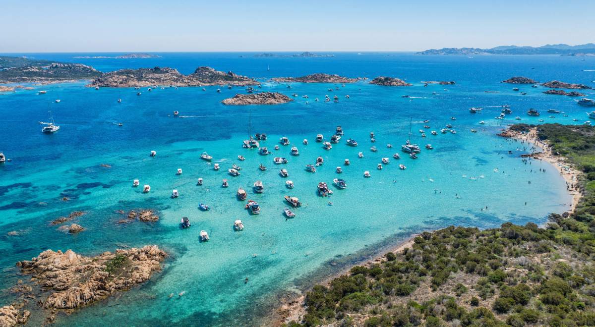Vista aérea de aguas turquesas y pequeñas calas en el norte de Cerdeña, con decenas de barcos fondeados.