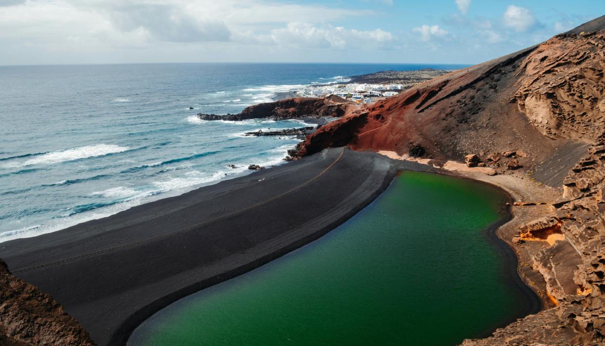 Charco verde junto a una playa de arena negra y acantilados volcánicos en Lanzarote