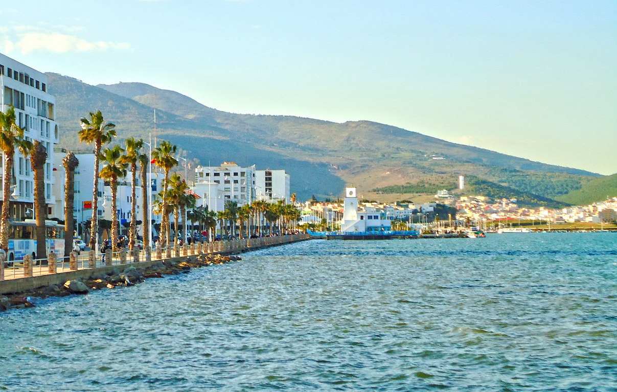 Paseo marítimo de Nador junto al mar, con palmeras, edificaciones blancas y montañas al fondo