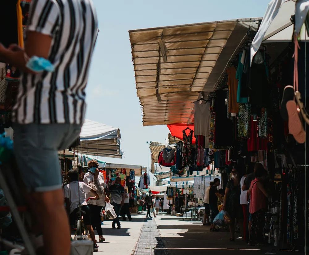Ambiente local en un mercado callejero de Sicilia durante la primavera, con puestos de ropa y gente paseando.