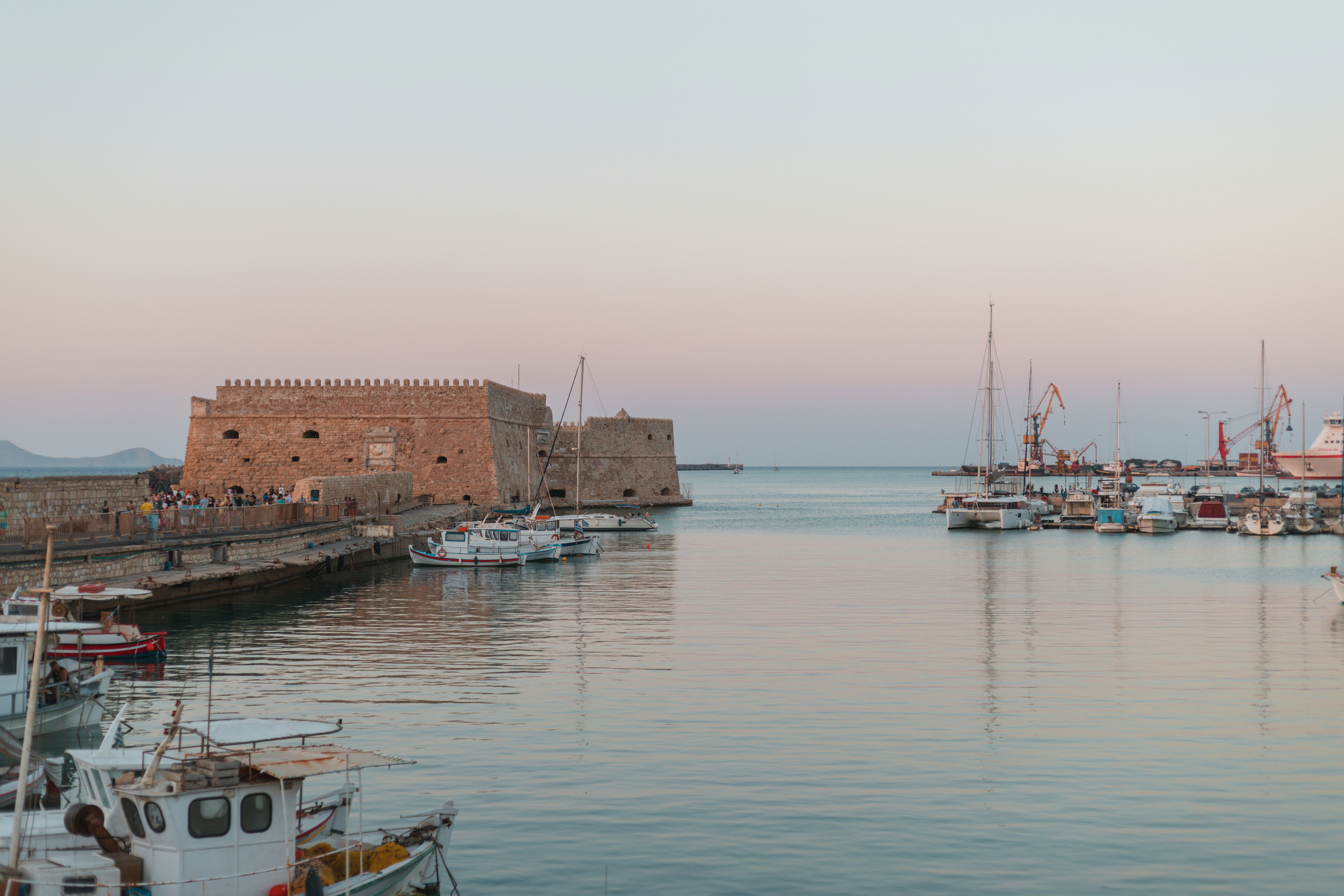 Der Hafen von Heraklion auf Kreta. Einige Fischerboote liegen bei ruhiger See am Hafen, das Licht ist sanft im Sonnenaufgang.