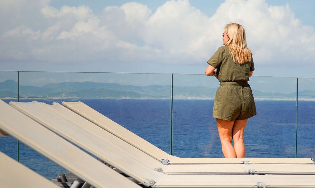 Mujer observando el mar desde la cubierta de un ferry con tumbonas vacías y vistas a la costa de Mallorca