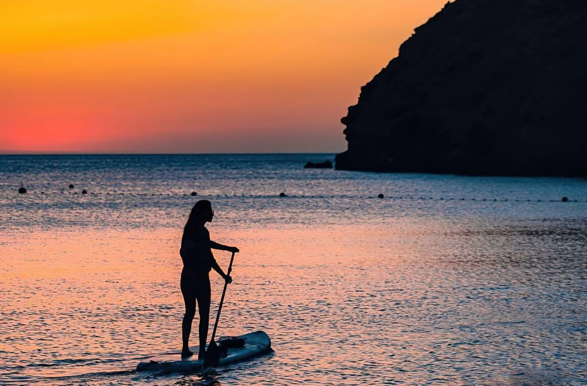 Mujer practicando paddle surf al atardecer en las playas de Canarias.