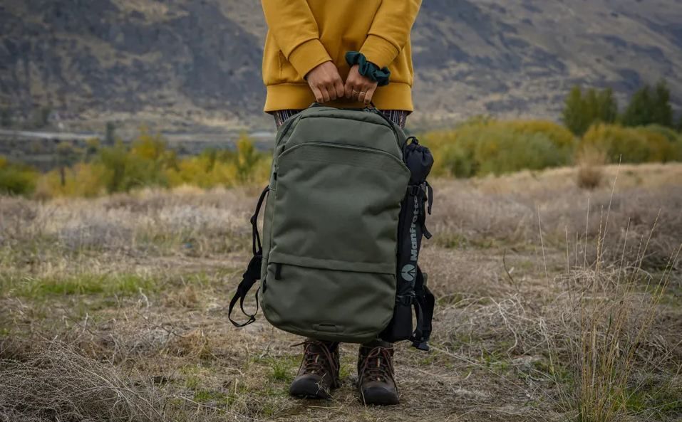 Persona de pie sujetando una mochila grande de viaje en un paisaje de campo.