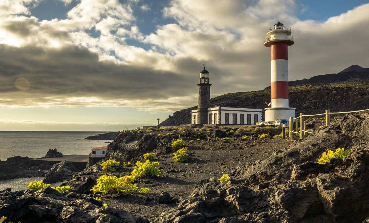 Faro situado sobre roca volcánica con nubes bajas en la costa de La Palma