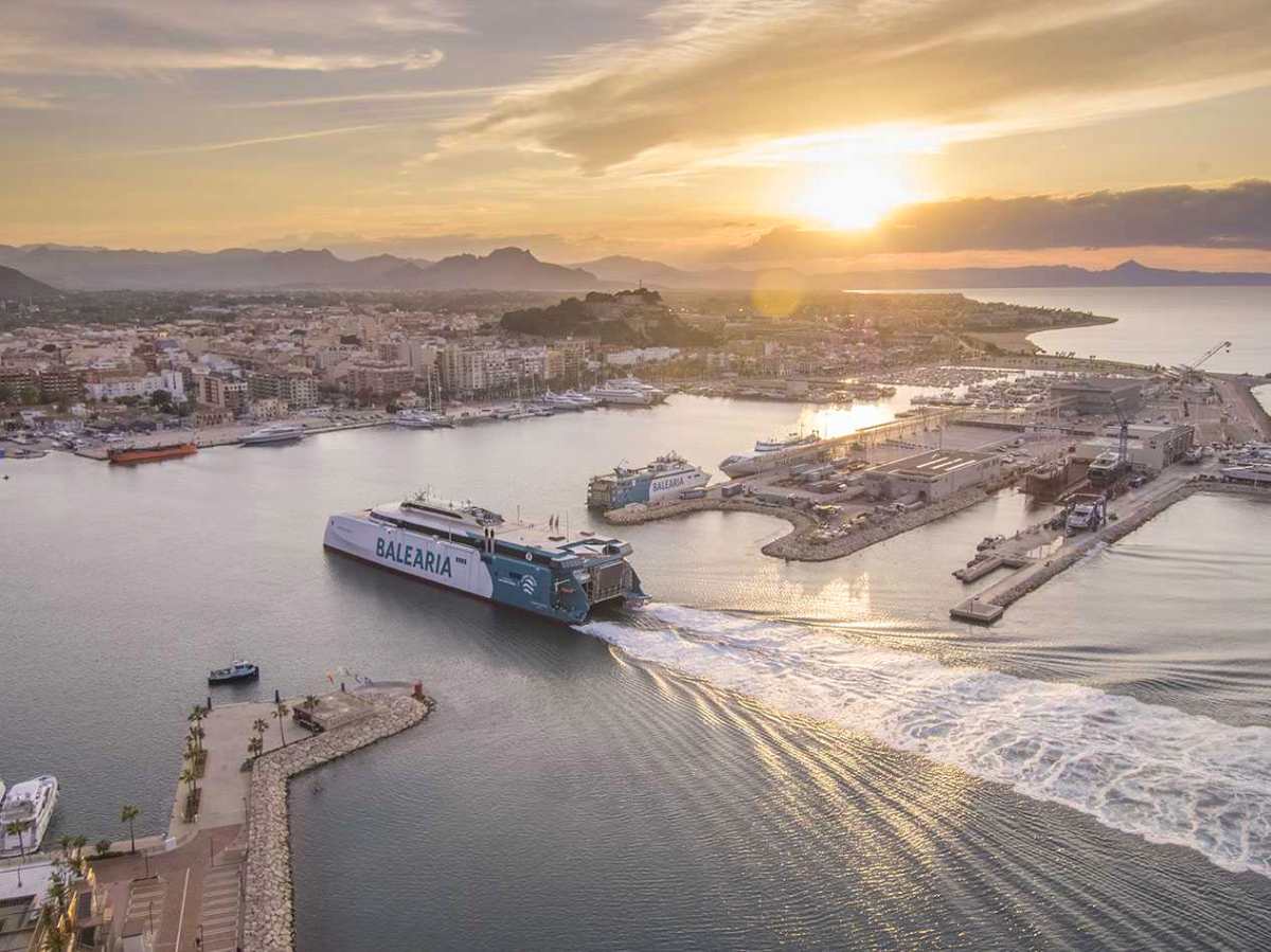 Ferry de Baleària zarpando del puerto de Dénia al atardecer con la ciudad y el castillo al fondo