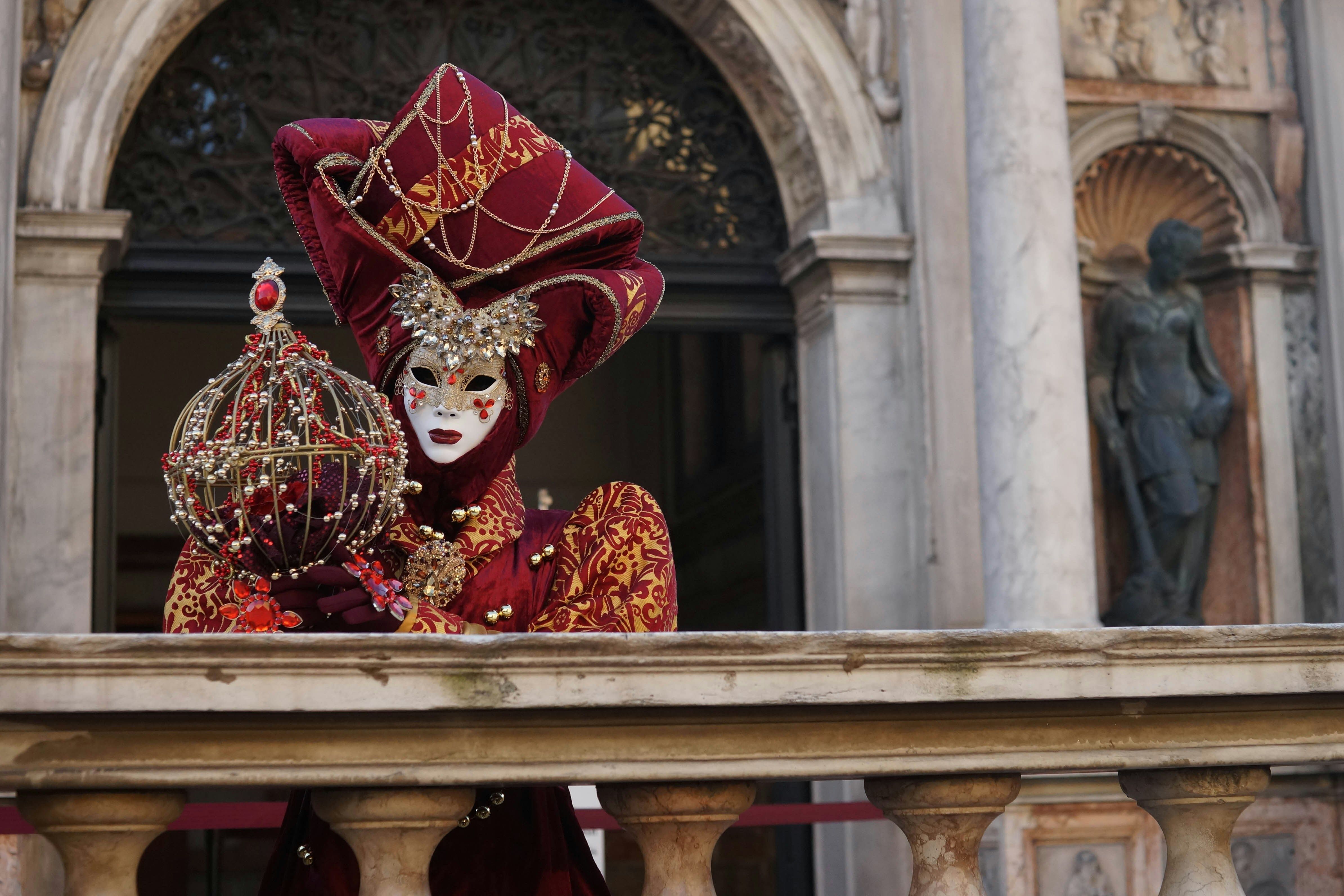 Una maschera tradizionale veneziana si affaccia al balcone di un palazzo antico.