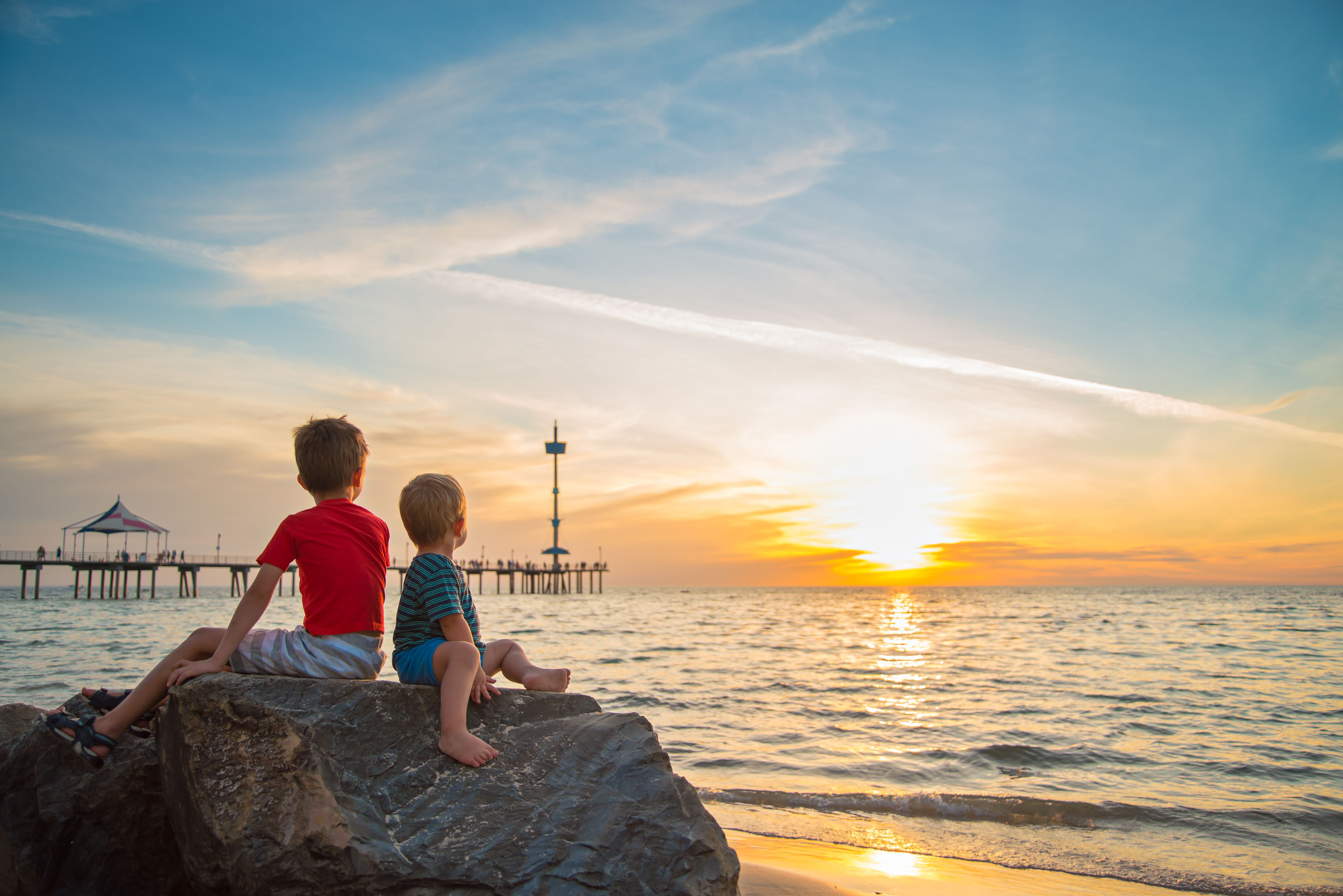 two children sat on a rock watching the sunset