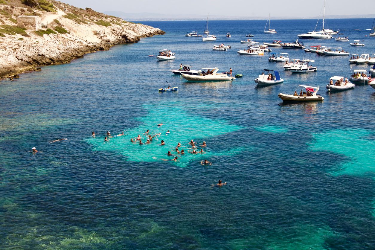 Bagnanti e barche a vela al largo di Levanzo, Egadi, Sicilia.
