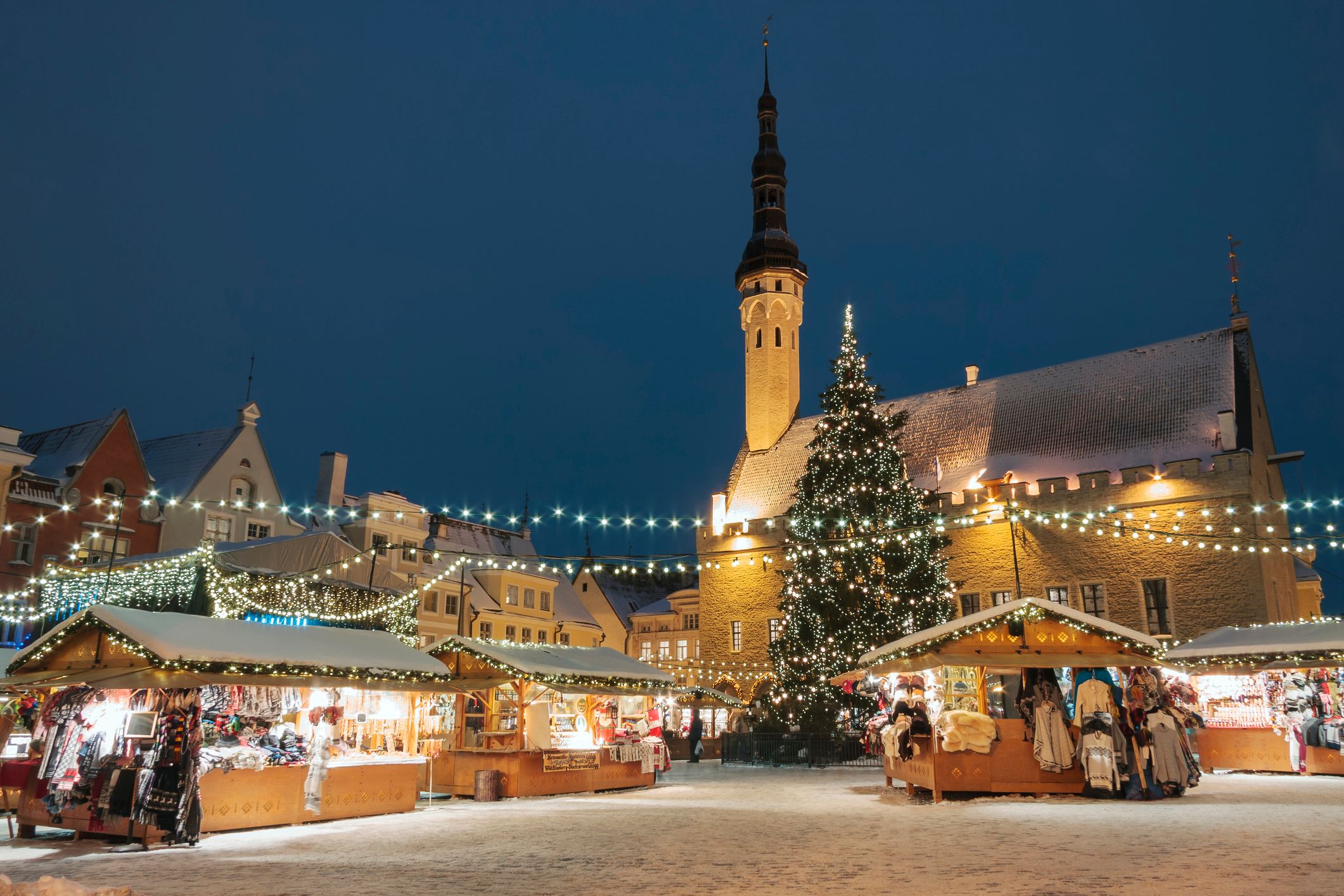 Der Weihnachtsmarkt in Tallinn, Estland. Man sieht das Rathaus, den großen geschmückten Weihnachtsbaum und ein paar Hütten. Lichterketten sind über den Rathausplatz gespannt.