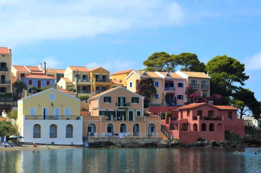 Casas de colores pastel junto al mar en Assos, Kefalonia, rodeadas de pinos y con reflejos en el agua