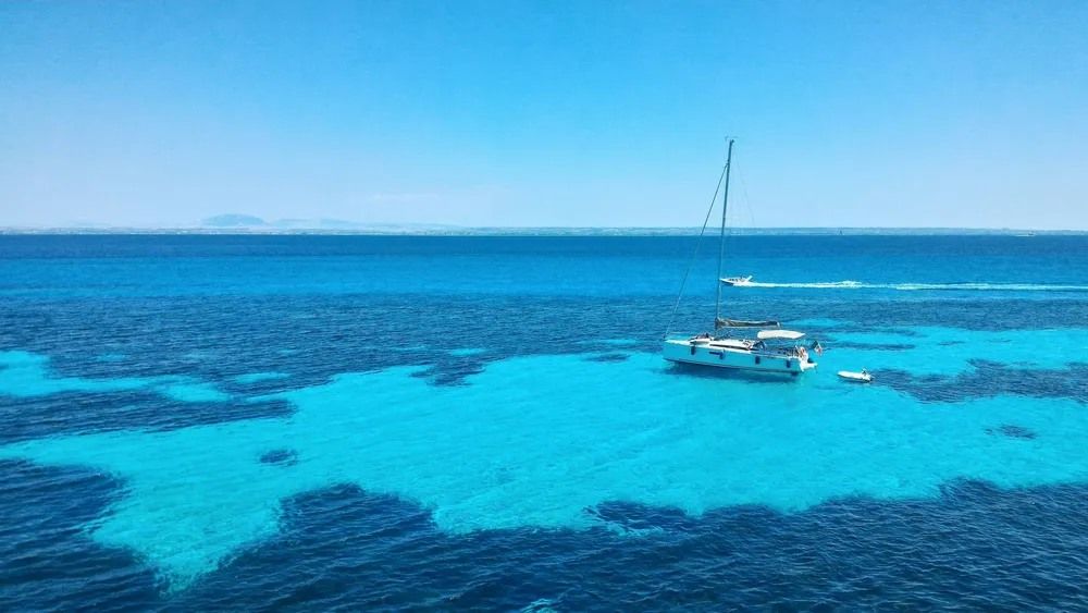 Aguas turquesas de la isla de Favignana en Sicilia con barcos navegando en un día soleado de primavera.