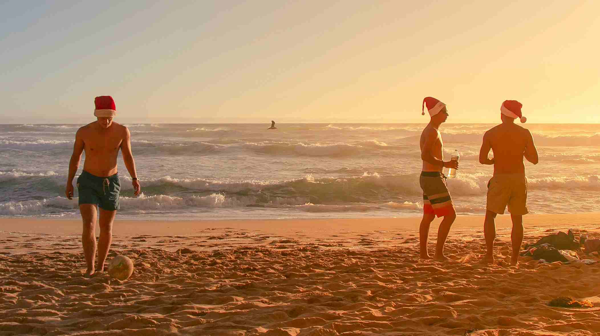 Jóvenes en la playa al atardecer con gorros de Navidad y el mar de fondo